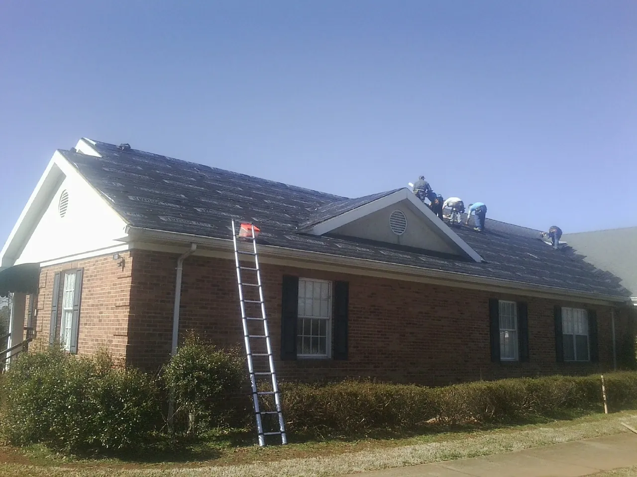 Crew tearing shingles off a brick ranch roof with a ladder set — Metal Roof Repair work by our crew in Verona
