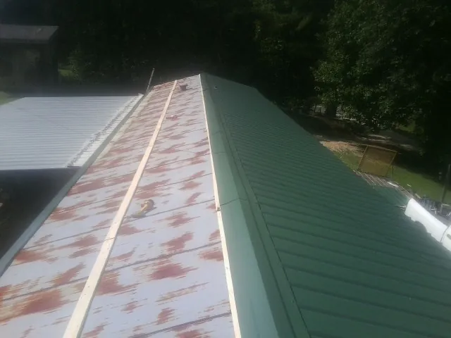 Old rusted panels beside newly installed green metal roofing — Wind Damage Roof Repair by Roofing Brothers in Verona