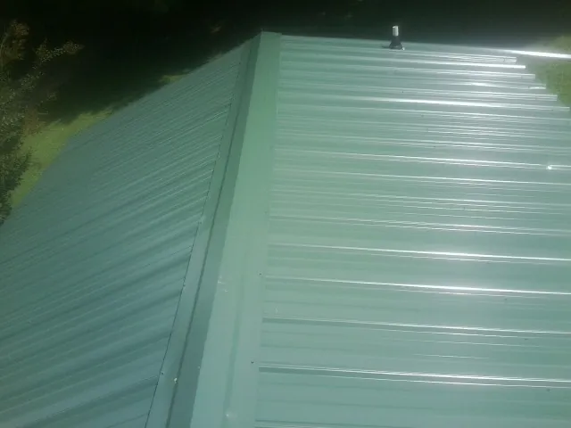 New green metal panels meeting at the ridge of a roof — Flat Roof Repair work by our crew in Verona